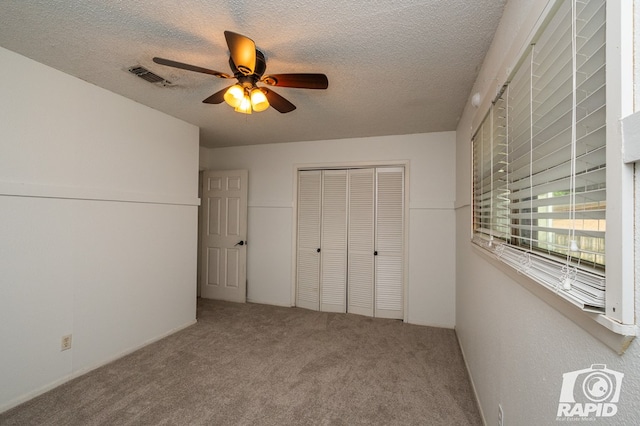 unfurnished bedroom with a ceiling fan, a textured ceiling, visible vents, carpet floors, and a closet