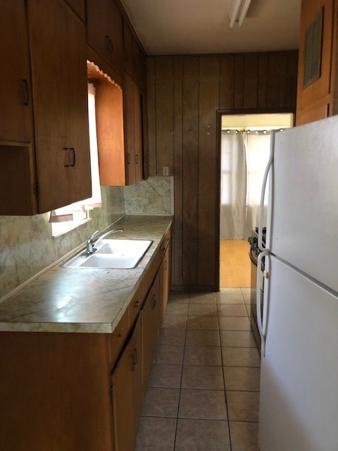 kitchen featuring white refrigerator, light tile patterned flooring, sink, and wooden walls