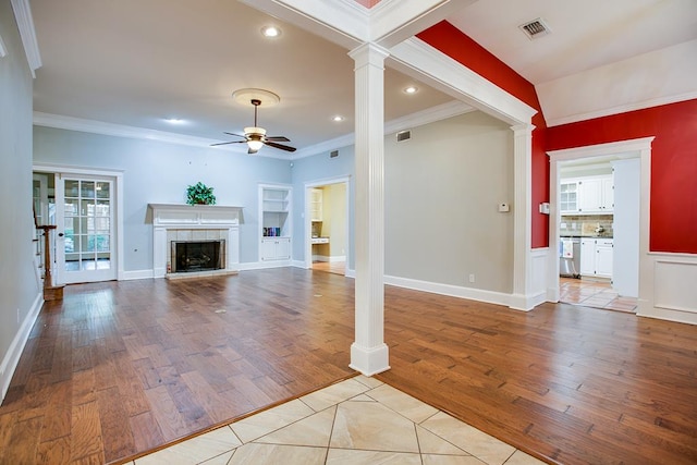 5413 Bent Oak Ct, San Angelo, TX 76904 - unfurnished living room featuring a ceiling fan, ornate columns, a tiled fireplace, crown molding, and light wood-style flooring