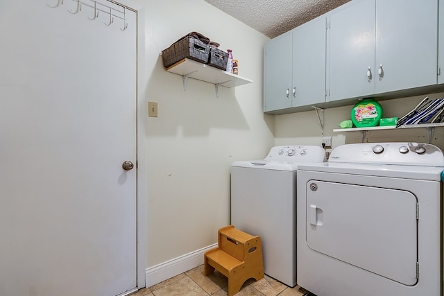 laundry area with cabinets, washer and dryer, a textured ceiling, and light tile patterned flooring