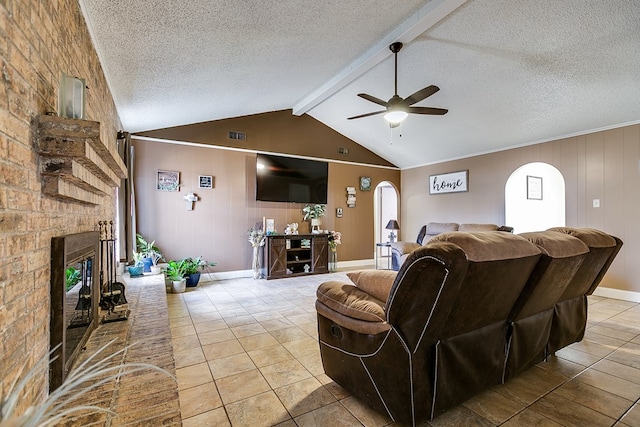 living room with a brick fireplace, ceiling fan, a textured ceiling, and light tile patterned flooring