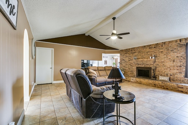 tiled living room with ceiling fan, a fireplace, a textured ceiling, and vaulted ceiling with beams