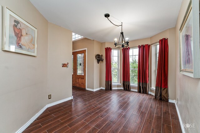 unfurnished room with baseboards, a chandelier, and dark wood finished floors