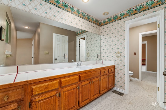 bathroom featuring toilet, wallpapered walls, vanity, and baseboards