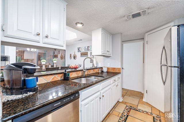 kitchen with visible vents, a sink, dark stone countertops, stainless steel appliances, and white cabinetry