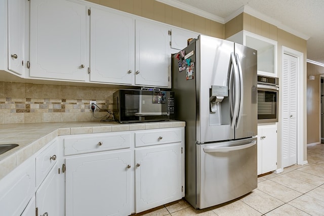 kitchen with appliances with stainless steel finishes, white cabinetry, ornamental molding, tile counters, and light tile patterned floors