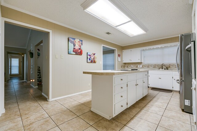 kitchen with light tile patterned floors, light countertops, ornamental molding, freestanding refrigerator, and a sink