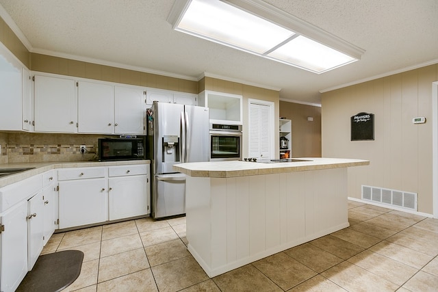 kitchen with light tile patterned flooring, appliances with stainless steel finishes, white cabinetry, a center island, and crown molding