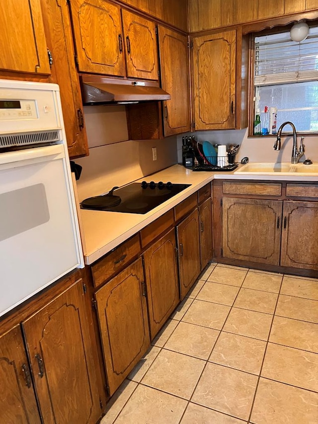 kitchen with light tile patterned flooring, black electric cooktop, sink, and white oven