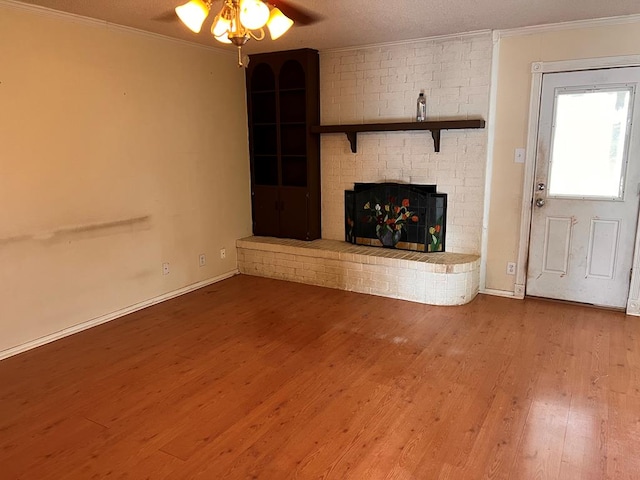 unfurnished living room featuring ornamental molding, a brick fireplace, wood-type flooring, and a textured ceiling