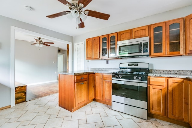 kitchen featuring a ceiling fan, appliances with stainless steel finishes, brown cabinetry, and a peninsula