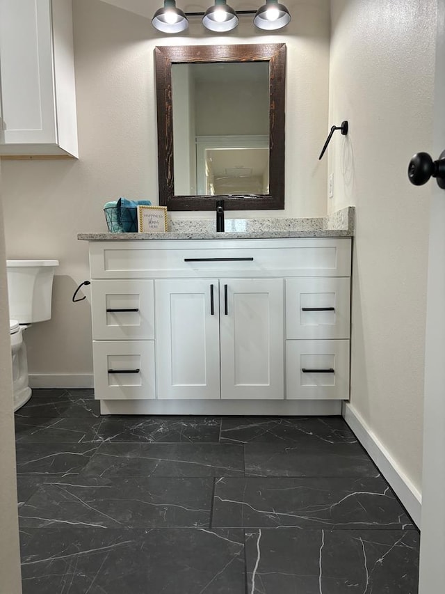 half bath with vanity, toilet, baseboards, and marble finish floor