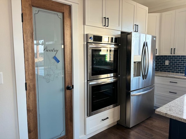 kitchen featuring dark wood-type flooring, light stone counters, decorative backsplash, stainless steel appliances, and white cabinetry