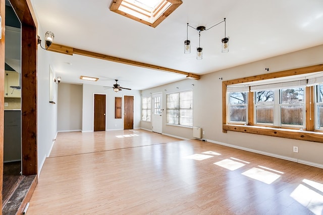 unfurnished living room featuring beamed ceiling, radiator heating unit, light hardwood / wood-style floors, and a skylight