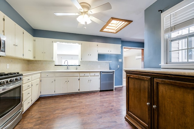 kitchen with dark wood-type flooring, sink, a skylight, stainless steel appliances, and decorative backsplash