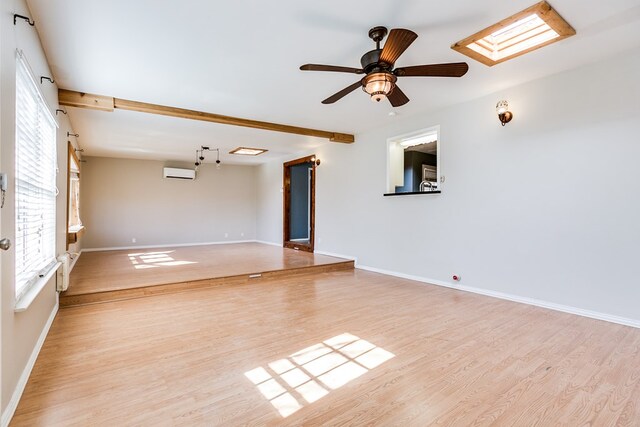 spare room featuring a skylight, beam ceiling, light hardwood / wood-style flooring, and a wall unit AC