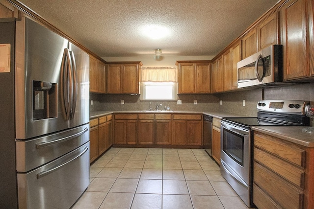 5905 Stratford Ave, San Angelo, TX 76901 - kitchen featuring brown cabinetry, decorative backsplash, a textured ceiling, light tile patterned floors, and stainless steel appliances