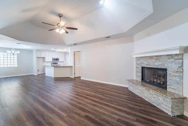 unfurnished living room featuring dark hardwood / wood-style flooring, a stone fireplace, a raised ceiling, and ceiling fan with notable chandelier