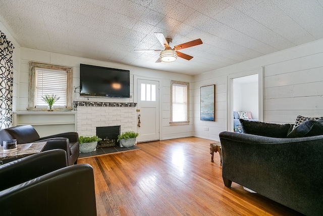 living area featuring wood walls, wood finished floors, ceiling fan, and a brick fireplace