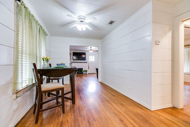 dining area with light wood-style floors, a brick fireplace, a ceiling fan, visible vents, and wood walls