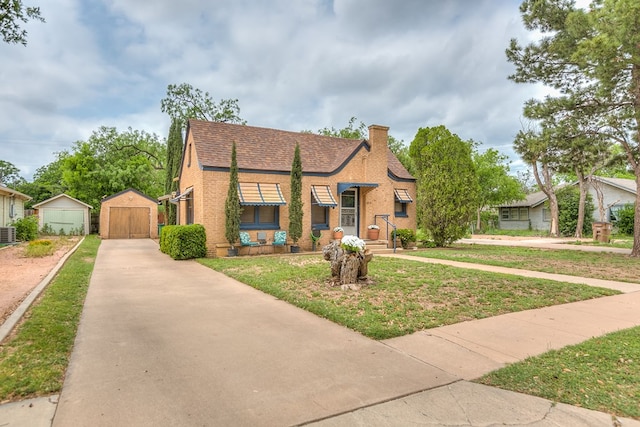tudor house with a front yard, brick siding, an outdoor structure, a detached garage, and a chimney