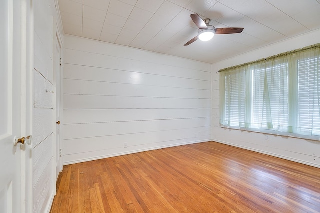 empty room with a ceiling fan, baseboards, wood walls, and light wood-type flooring