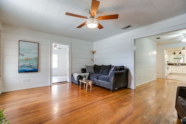 living room with wood walls, ceiling fan, light wood-type flooring, and visible vents