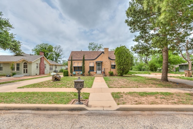 view of front of home featuring a chimney, brick siding, and a front yard
