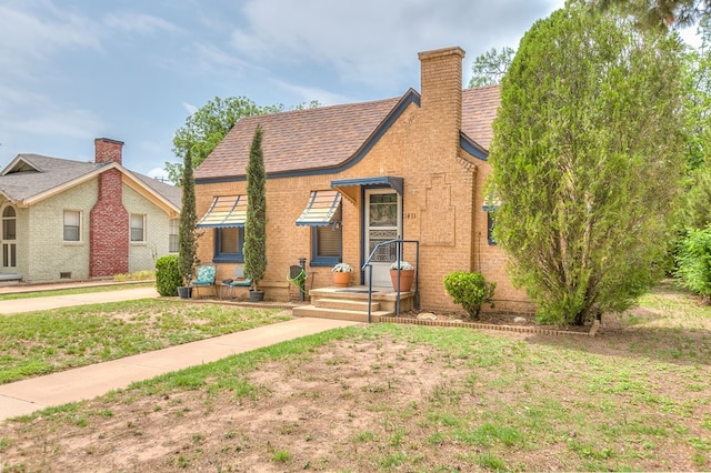 view of front of property with a chimney, brick siding, and a front lawn
