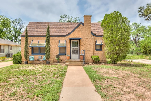 bungalow-style house with a chimney, cooling unit, and a front yard