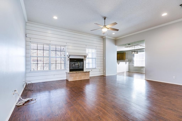 unfurnished living room featuring wooden walls, a tiled fireplace, ceiling fan, crown molding, and a textured ceiling