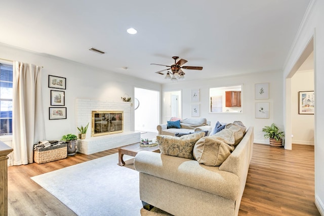 living area featuring light wood-type flooring, a ceiling fan, baseboards, a brick fireplace, and recessed lighting