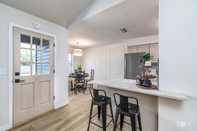 1702 Parkview Dr, San Angelo, TX 76904 - kitchen with freestanding refrigerator, light wood-style flooring, a breakfast bar, a peninsula, and light stone counters