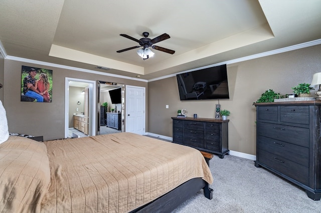 bedroom with ceiling fan, a tray ceiling, crown molding, light carpet, and ensuite bath