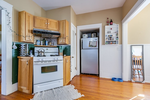 kitchen featuring fridge, white gas stove, light hardwood / wood-style floors, and decorative backsplash