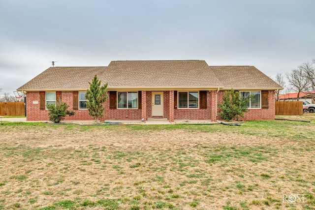 ranch-style house featuring brick siding, a shingled roof, a front lawn, and fence