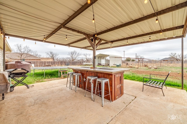 view of patio featuring a trampoline, outdoor dry bar, and fence