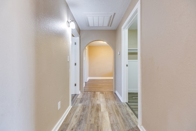 hallway with a textured ceiling and light hardwood / wood-style flooring