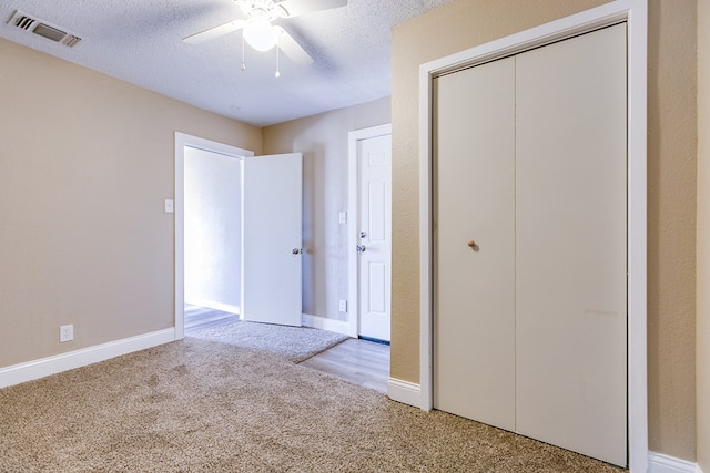 unfurnished bedroom featuring ceiling fan, light colored carpet, a closet, and a textured ceiling