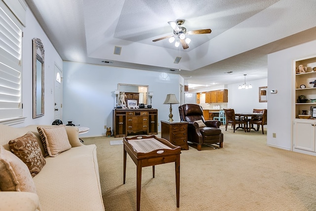 carpeted living room with ceiling fan with notable chandelier, a textured ceiling, a raised ceiling, and built in shelves