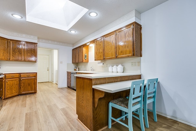 kitchen featuring dishwasher, a kitchen breakfast bar, kitchen peninsula, a textured ceiling, and light hardwood / wood-style flooring