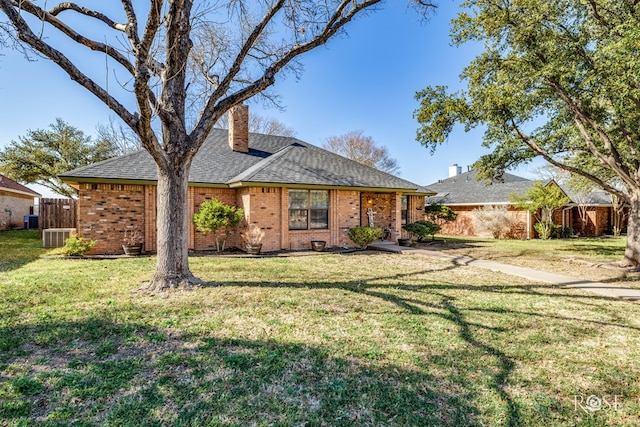 view of front facade with brick siding, a shingled roof, fence, a chimney, and a front yard