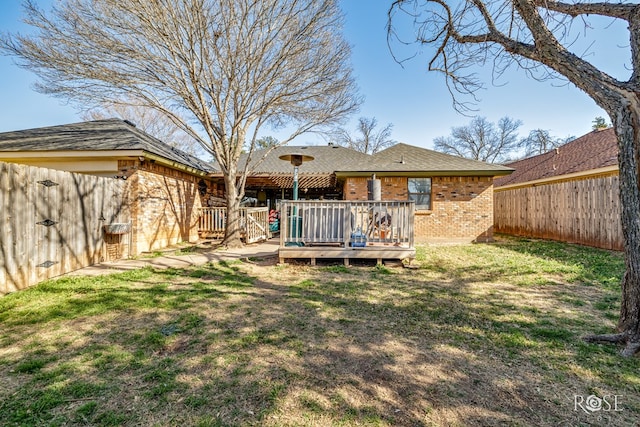 rear view of house with a fenced backyard, brick siding, a wooden deck, and a lawn