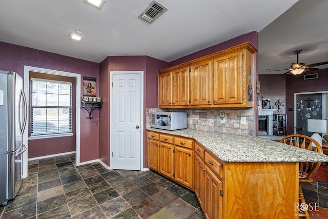 kitchen featuring a breakfast bar, visible vents, white microwave, freestanding refrigerator, and a peninsula