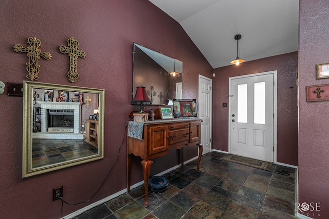 foyer featuring vaulted ceiling, a brick fireplace, baseboards, and stone tile floors