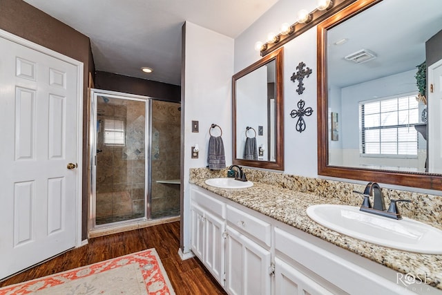 full bath with double vanity, a sink, a shower stall, and wood finished floors