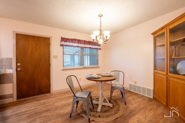 dining area with an inviting chandelier, light hardwood / wood-style flooring, and a textured ceiling