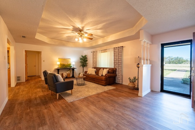 living room featuring hardwood / wood-style floors, a tray ceiling, a textured ceiling, and ceiling fan