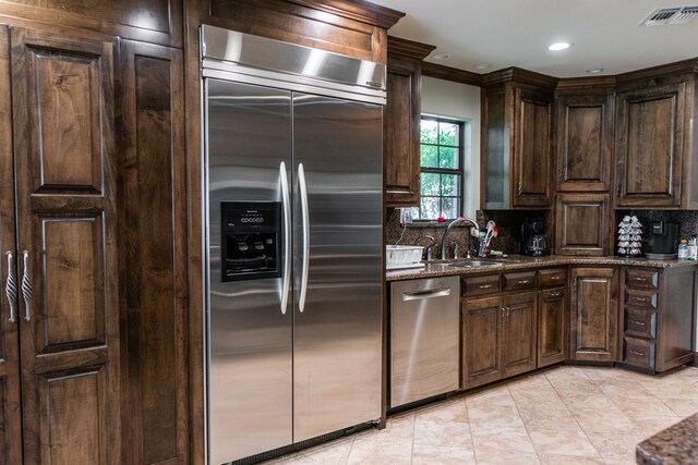 5213 Green Valley Trl, San Angelo, TX 76904 - kitchen with appliances with stainless steel finishes, decorative backsplash, dark brown cabinets, dark stone countertops, and light tile patterned floors