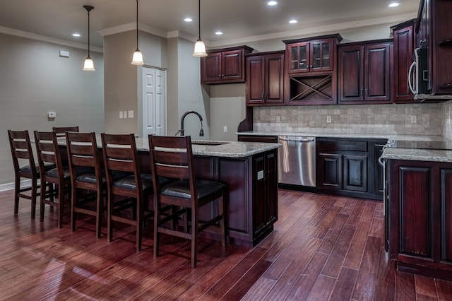 kitchen featuring pendant lighting, appliances with stainless steel finishes, a kitchen island with sink, backsplash, and light stone countertops